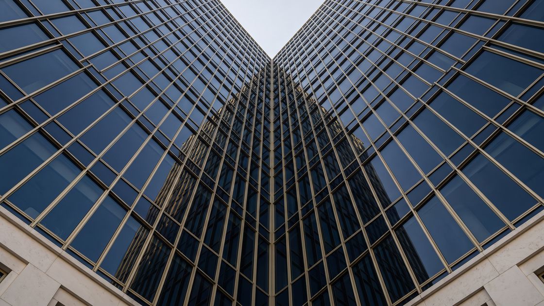Two planes of dark glass and slender metal mullions converging against a pale sky.